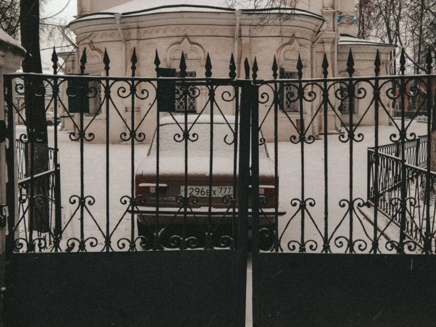 Iron gate with a vintage car, snowy courtyard, and historic building facade.